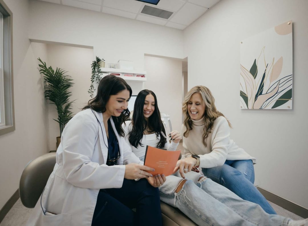 Doctor reviewing information on a tablet with a teenage patient and her mother in a medical office.
