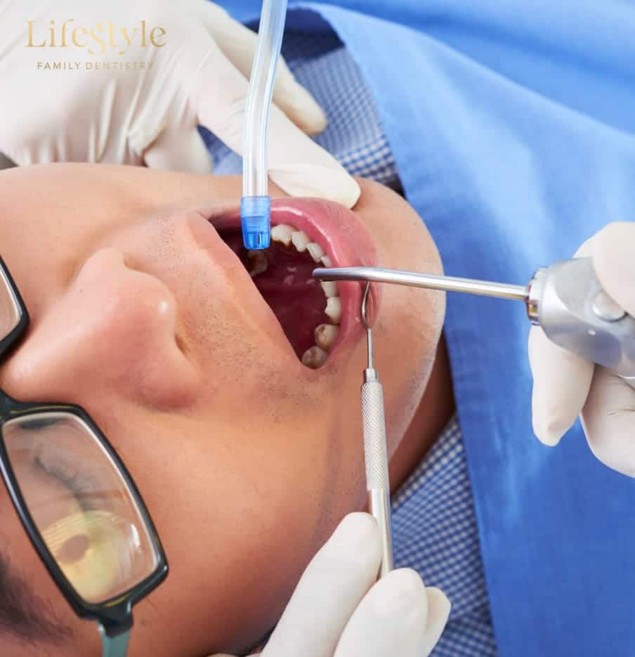 Dentist performing a dental procedure using suction and instruments while the patient lies in a treatment chair.