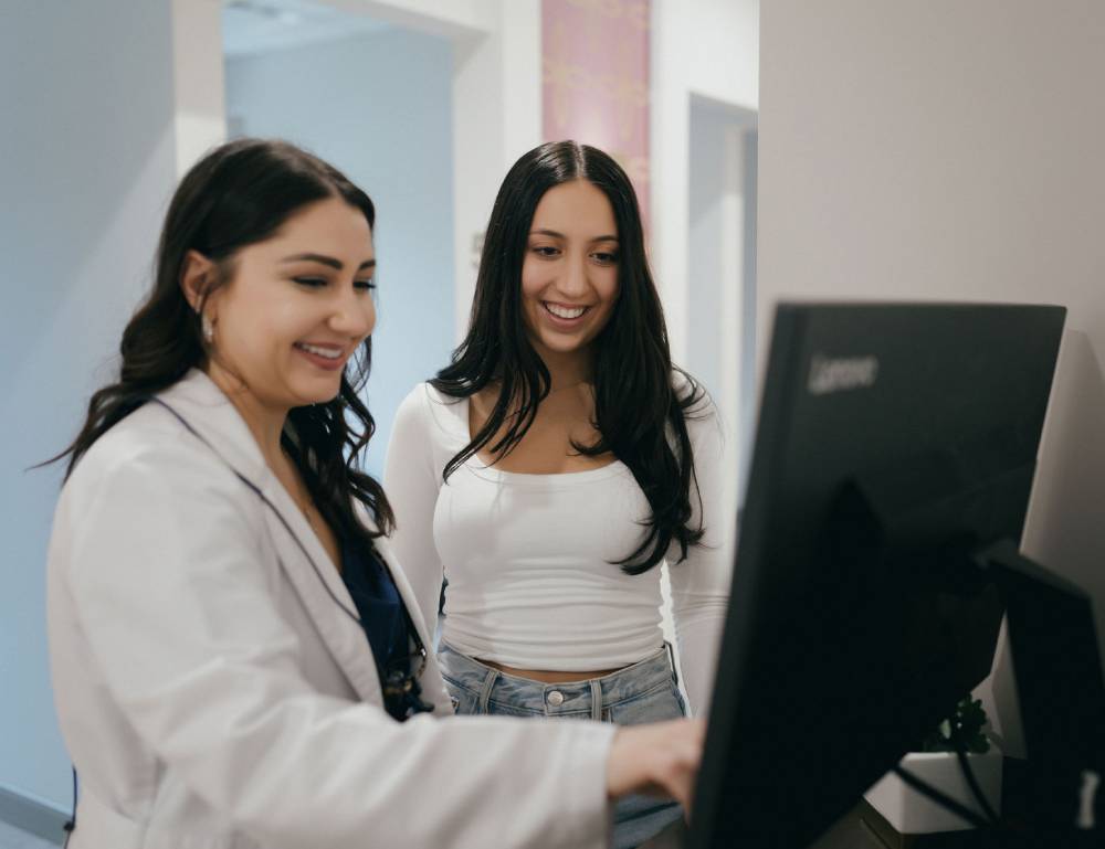 Doctor showing medical information on a computer screen to a smiling young woman during a consultation.