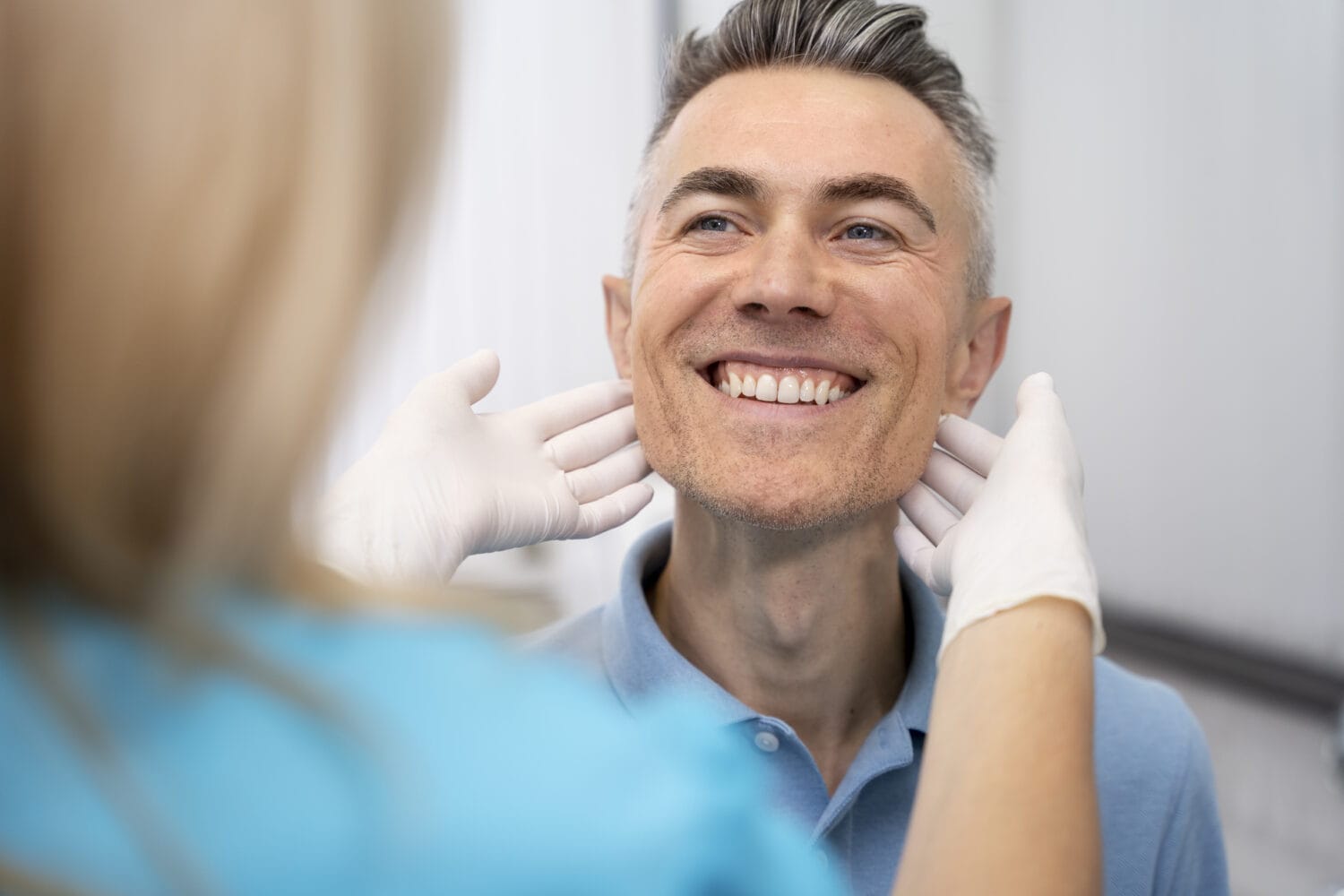 Doctor wearing gloves performing a neck examination on a smiling male patient during a routine medical checkup.