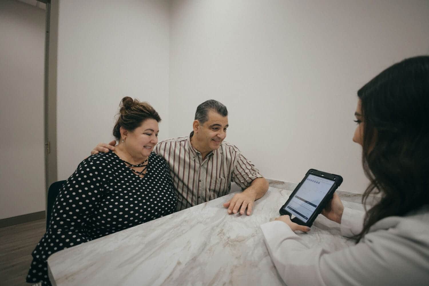 Dentist reviewing a treatment plan on a tablet with a smiling couple during a consultation in a dental office.