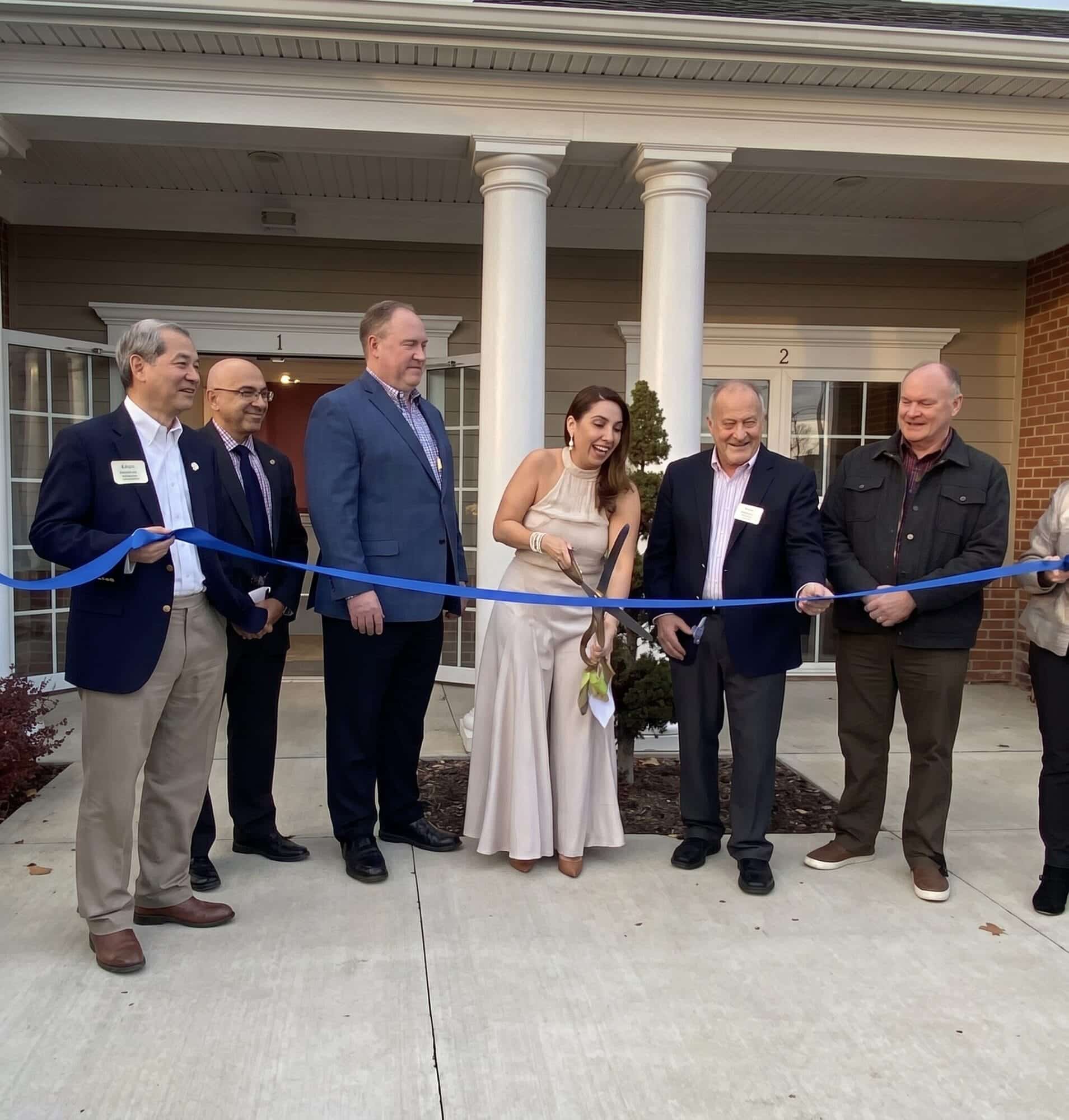 Group of people participating in a ribbon-cutting ceremony outside a building entrance