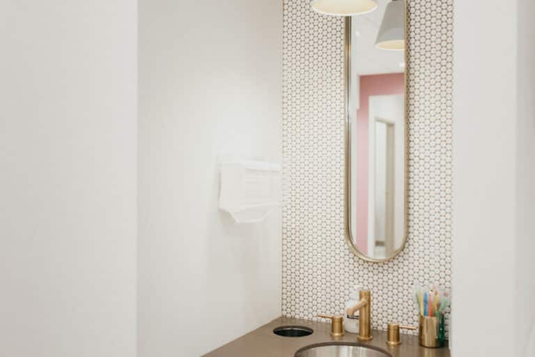 Modern dental office sink area with a mirror, soap, mouthwash, and stylish backsplash